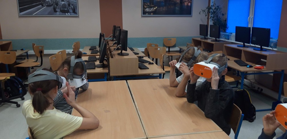 Grupa 4 uczniów siedzi przy stole. Wszyscy mają okulary VR założone na głowę. 