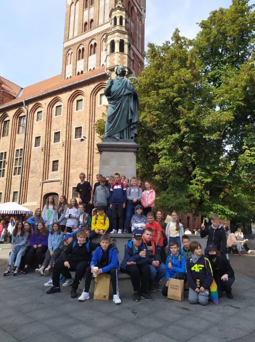Uczniowie stoją na tle pomnika Adama Mickiewicza w Toruniu