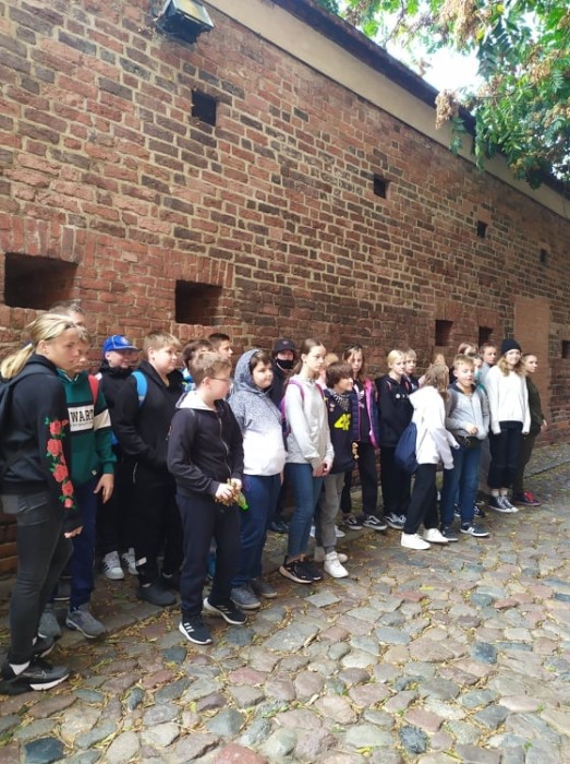 Uczniowie stoją przy ścianie krzywej wieży w Toruniu